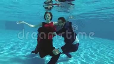 一对相爱的夫妇，新娘和新郎，穿着婚纱在游泳池的水下游泳。 他们微笑，享受，玩耍